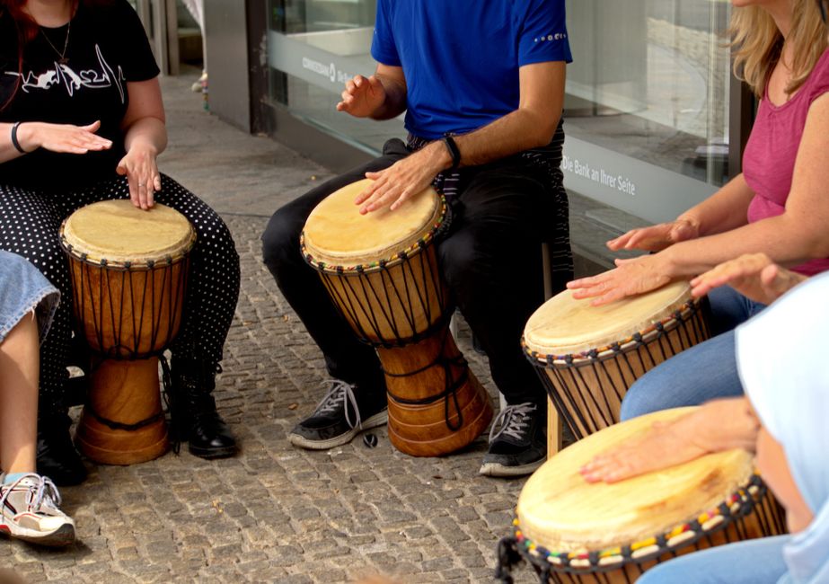 Adults playing African djembes outdoors, creating rhythm and music in a public space.