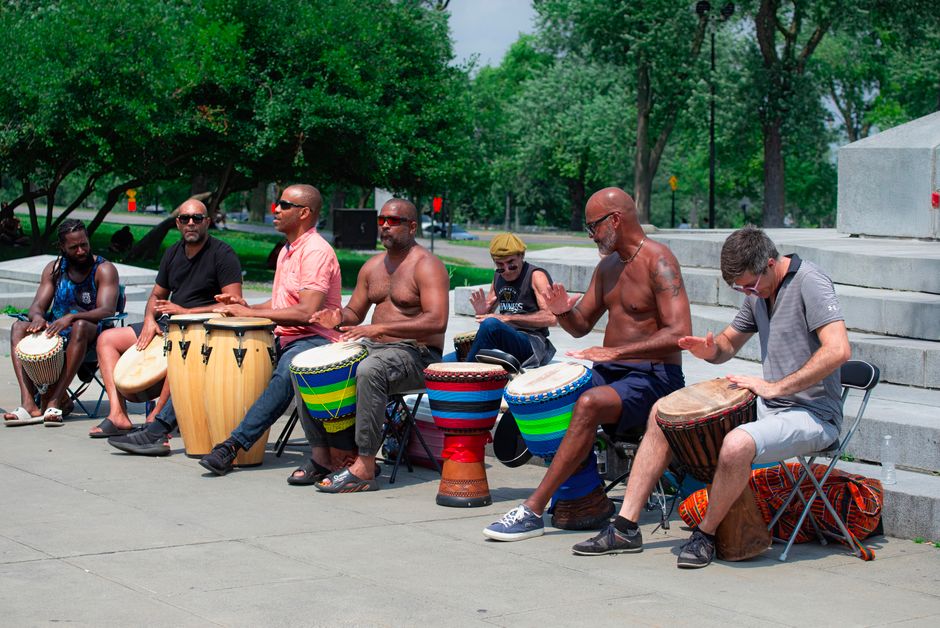 Group of diverse adults playing drums outdoors, enjoying a lively drum circle in a sunny park.